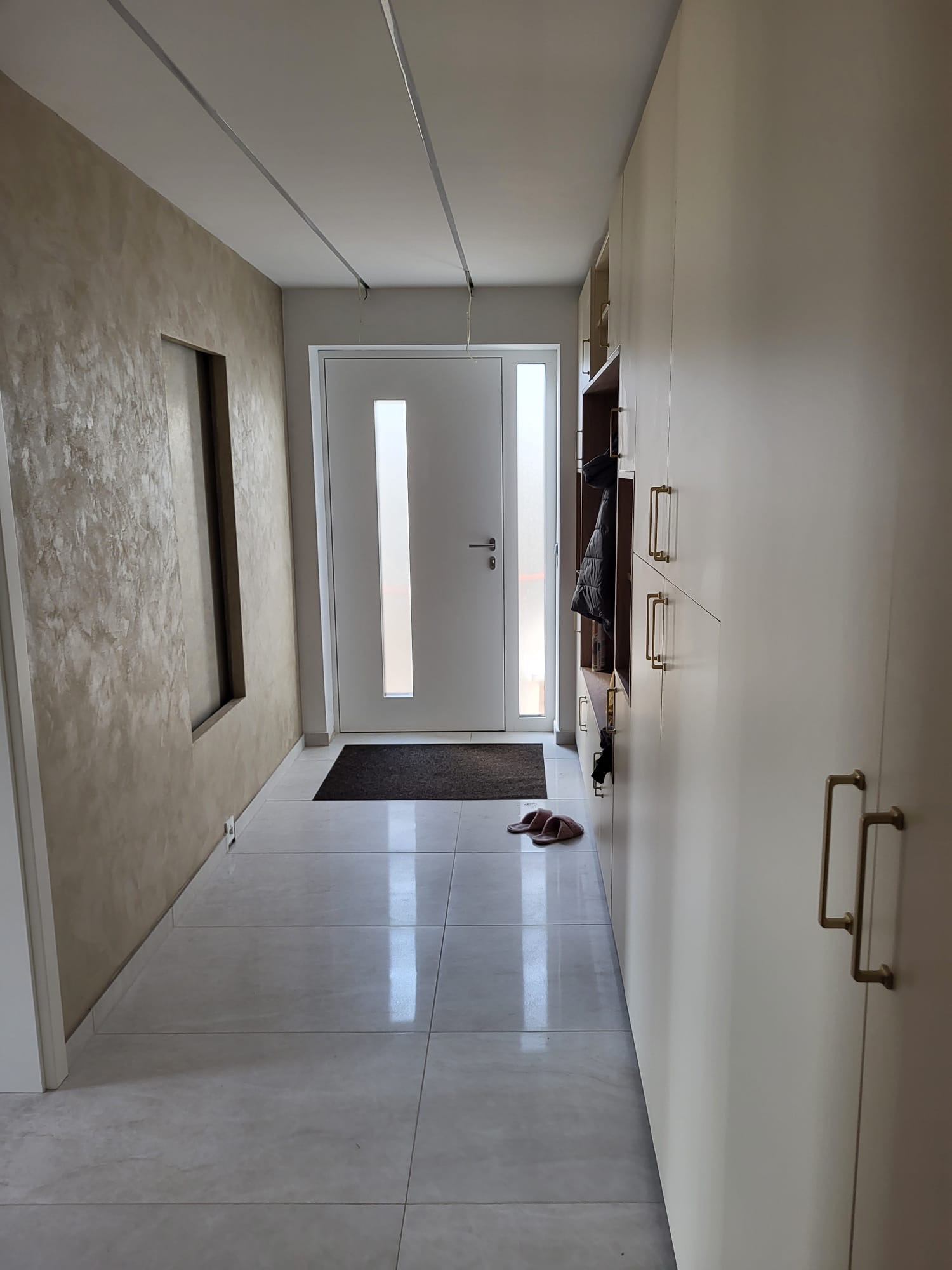 Eingangsflur mit Travertin-Spachteltechnik an der Wand, Wandnische und weißer Einbau-Garderobe
