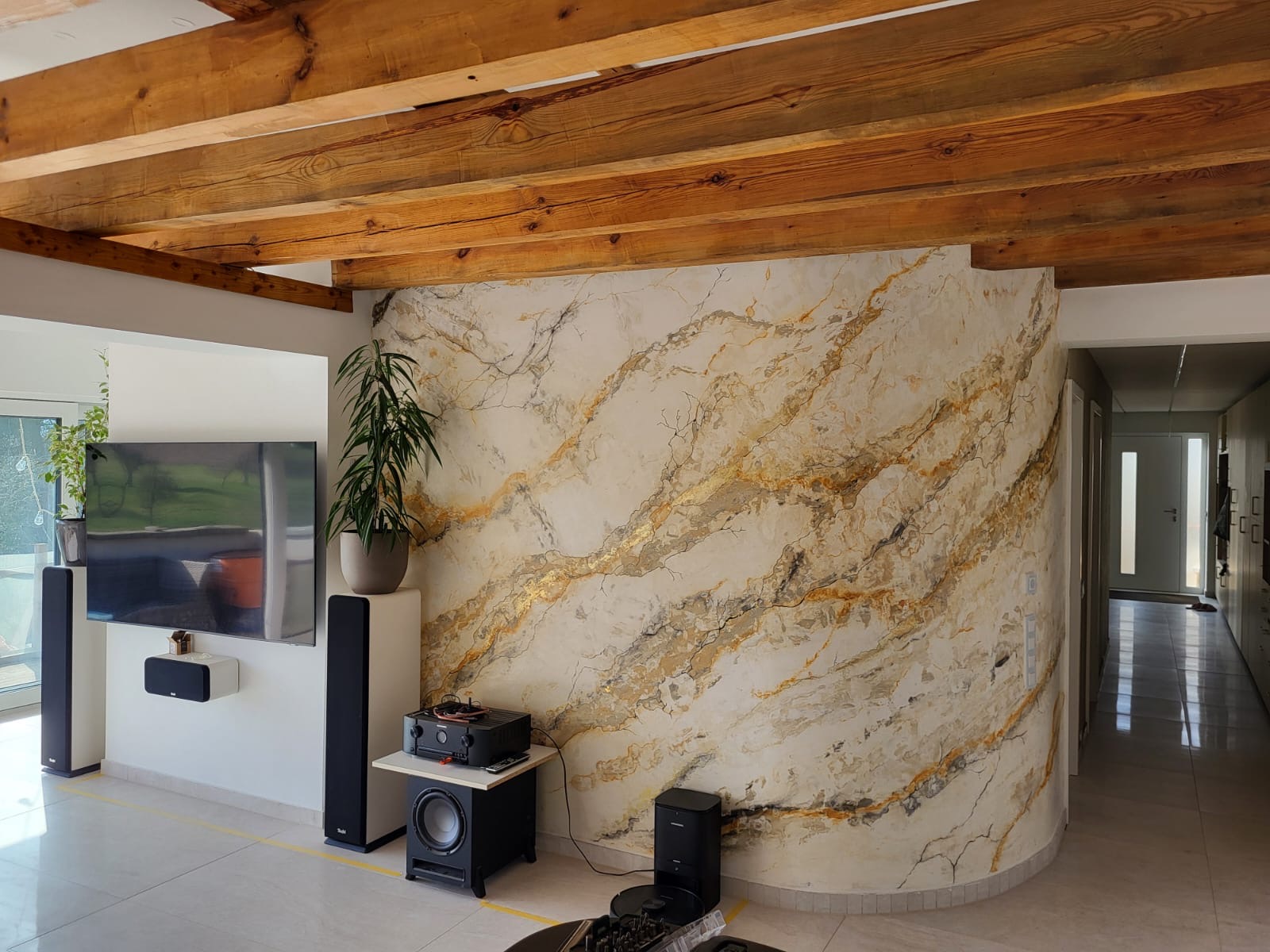 Geschwungene Innenwand in Marmor-Spachteltechnik mit goldenen Adern in modernem Wohnzimmer mit Holzbalkendecke